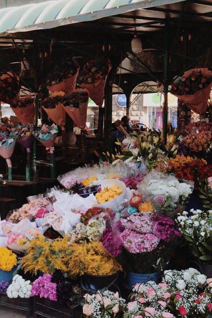 A vibrant display of fresh flowers at a florist stall, featuring a variety of colourful arrangements including roses, lilies, and carnations in shades of pink, white, yellow, and red. The flowers are