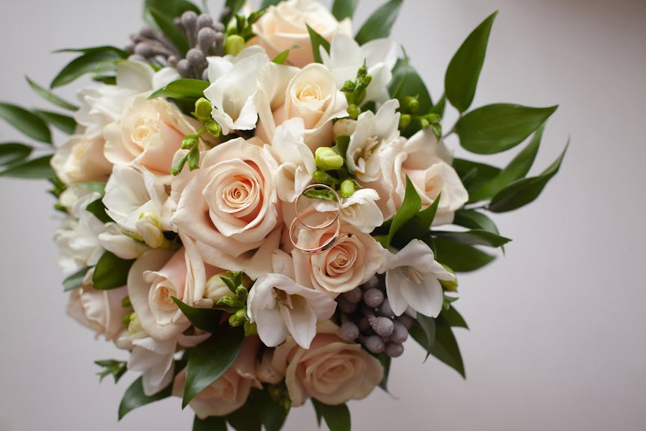 A close-up image of a floral bouquet featuring soft pink roses with tightly curled petals, complemented by white freesias with delicate, trumpet-shaped blooms, and clusters of small purple berries. Th