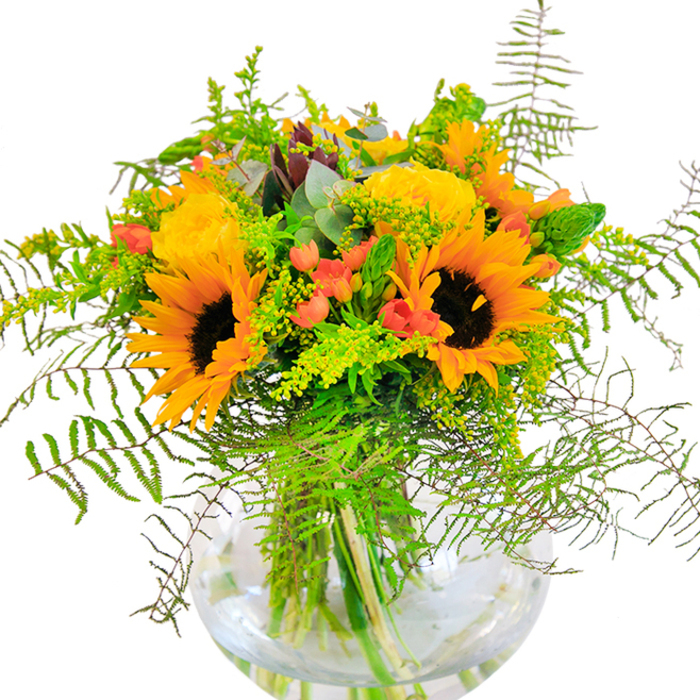 The essence of late summer in Greenford is perfectly captured in this radiant bouquet, arranged with attention to colour, detail, and texture. Dominating the display are soaring sunflowers, their cheerful faces wide open and inviting beneath the soft light, petals unfurling in a celebration of sunlight and promise. Plush yellow garden roses nestle among them, each bloom crafted in intricate layers, lending a classic romance that nods to the tradition of English floristry. Red hypericum berries, shiny and robust, are scattered throughout-like the last jewels of the season found on morning walks around Greenford's Brent Valley Park. Stretching outwards, verdant ferns and trailing greenery gently lower the bouquet's silhouette, adding lively movement and a touch of wild beauty. Wispy spikes of filler in green and dotted with tiny yellow blossoms provide additional interest and texture, while muted eucalyptus leaves anchor the colour scheme with their cool, refreshing hue. All of this is gathered in a clear, spherical glass vase, which elevates the natural beauty of submerged, intertwining stems and lends contemporary flair to the whole composition. Sunbeams filtering across a Greenford kitchen table highlight every petal and berry, casting a gentle play of shadow and light across the vase. The gentle fragrance recalls local fields after summer rain, making this arrangement ideal for meaningful celebrations, thoughtful gifts, or bringing seasonal joy into any Greenford home.