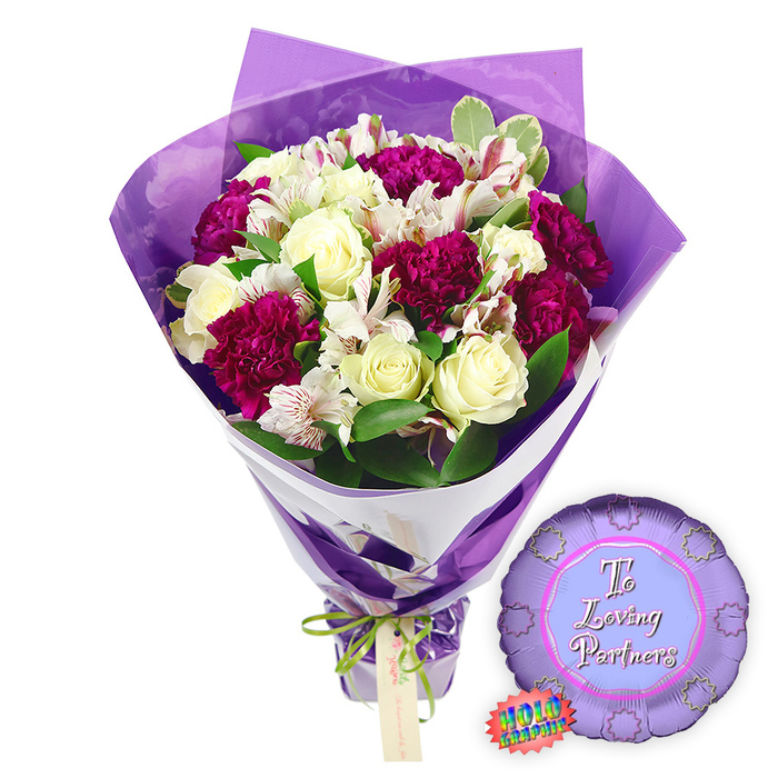 A carefully styled romantic bouquet and balloon combination is presented against a crisp white background, as if just prepared on the workbench at Greenford Flowers before heading out for local delivery. The bouquet itself is rich and rounded, built around a central cluster of creamy white roses. Each rose is at that perfect early stage of opening, with petals curled inward in tight, velvety spirals that speak of freshness and lasting beauty. Tucked among them are deep magenta and burgundy carnations, their densely frilled petals forming plush, cloud-like clusters, bringing depth, texture, and a sense of passionate colour to the design. Interlaced with the roses and carnations are white alstroemeria, or Peruvian lilies, their elegant trumpets spreading out to reveal fine reddish-brown stripes and speckles along the inner petals, a detail that adds refinement and interest on closer inspection. Surrounding this medley of blooms is a layer of vibrant greenery, some leaves solid and glossy, others lightly variegated, giving the arrangement a full, garden-fresh character reminiscent of the leafy corners of Greenford and its surrounding parks. The flowers are wrapped in two distinct layers: an inner sheet of bright white paper, visible as a diagonal band that hugs the stems, and an outer sheath of translucent purple cellophane. This crinkled purple film rises above the blossoms, forming soft, luminous peaks that catch the light and echo the rich tones of the carnations. At the base, the stems are neatly drawn together and tied with a slim, bright green satin ribbon, knotted into a small bow with a light brown rectangular tag dangling gently, inviting a personalised dedication. To the right of the bouquet, resting on the white surface, a metallic purple foil balloon sparkles. It is round with a scalloped, rosette-like edge, and its centre circle is a softer shade of purple, inscribed with the words To Loving Partners in stylish pink script. A small rainbow holographic sticker near the bottom edge glints, hinting at the balloon's reflective finish. The image encapsulates a romantic, celebratory gift ideal for anniversaries, Valentine's Day, or thoughtful gestures of appreciation shared across Greenford.