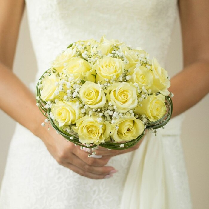 An artfully composed close-up in Greenford captures the essence of wedding beauty: a bride's carefully gathered bouquet, held against a dress of snow-white, textured fabric. Creamy yellow roses, each bloom perfectly formed and packed in a domed embrace, create a radiant focal point that gleams warmly in the gentle light-perhaps the same sunlight that graces Greenford's leafy open spaces. Wispy sprays of pure white baby's breath wind through the bouquet, imparting a gentle, airy presence and updating a timeless bridal tradition with local flair. Subtle whirls of dark green foliage or decorative wire frame the base, bestowing a finished look and underscoring the arrangement's classic silhouette. The bride's hands, one slipped with a glinting wedding band, nails immaculately manicured in blush tones, suggest a mix of serene joy and anticipation. Behind, hints of intricate embroidery or lace on the wedding gown conjure up images of local ceremonies in South Greenford or elegant receptions beside the canal. The softly blurred backdrop guarantees that the brilliant florals and meaningful moment remain front and centre. This image, crafted with Greenford's celebrated attention to detail, is ideal for inspiring couples seeking memorable bridal blooms reflective of the community's warmth and artistry.