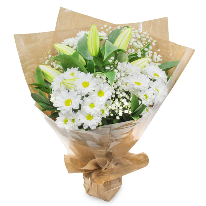 Captured against a stark white background, this refined bouquet of white and green flowers feels quietly dignified, as if prepared specially for a family in Greenford seeking a simple, heartfelt tribute. The main body of the arrangement is composed of white daisy-like chrysanthemums, their petals clean and unblemished, fanning out in delicate layers around soft yellow-green centers. Packed generously together, they create a full, cushiony texture that feels protective and gentle, a natural focal point for the eye. Rising among these daisies are several elongated lily buds, still firmly closed, their smooth outer petals shaded from pale green at the base to creamy white near the tips. They stand upright with subtle grace, bringing height, elegance, and an unspoken sense of hope for brighter days. Woven throughout the arrangement, fine sprays of white gypsophila contribute an airy, cloud-like softness, their tiny blossoms dotting the spaces between larger flowers like small points of light. Around the outside, glossy, deep green foliage frames the white blooms, giving structure and contrast reminiscent of the leafy edges of nearby Ravenor Park or the green verges along Greenford's residential roads. The stems are carefully bound together and wrapped in layers of natural brown kraft paper, its crinkled texture and warm tone adding an earthy, sincere character to the bouquet. Over this sits a layer of clear, slightly crinkled cellophane that reflects the light gently and protects the flowers while keeping every detail visible. The wrapping is neatly gathered and secured at the base, forming a conical, easy-to-hold shape suited to carrying into a quiet home, chapel, or hospital room. The overall impression is one of purity, calm, and heartfelt sympathy, making this bouquet an appropriate choice for memorials, funerals, or sending condolences throughout Greenford.