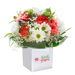 There's a spirited sense of celebration in this lush bouquet, poised in a sleek white gift bag and capturing the cheerful heart of flower giving in Greenford. Ruffled coral and vibrant red carnations exude softness and vitality, interlaced with pure white daisies whose golden-green centers offer an uplifting, sunny pop. Wisps of baby's breath float through the design, creating an airy, innocent ambiance akin to fresh blooms gathered from local parks. Glossy, deep green leaves embrace the arrangement, steady and grounding, while a touch of purple-tinged buds peeking on the left adds a whisper of curiosity and promise. The overall dome-shaped arrangement is both full and harmonious, each bloom placed with attentive care by Greenford's local experts. The sturdy, radiant ribbon handles atop the bag ensure the bouquet is ready for gifting-a thoughtful gesture for birthdays, milestones, or simply to lift someone's spirits on a quiet afternoon. Radiating joy and abundant freshness, this image mirrors the artistry and dedication found in every hand-delivered bouquet from Greenford Flowers.